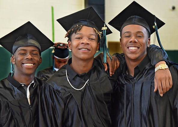 Three graduates smiling together in caps and gowns.
